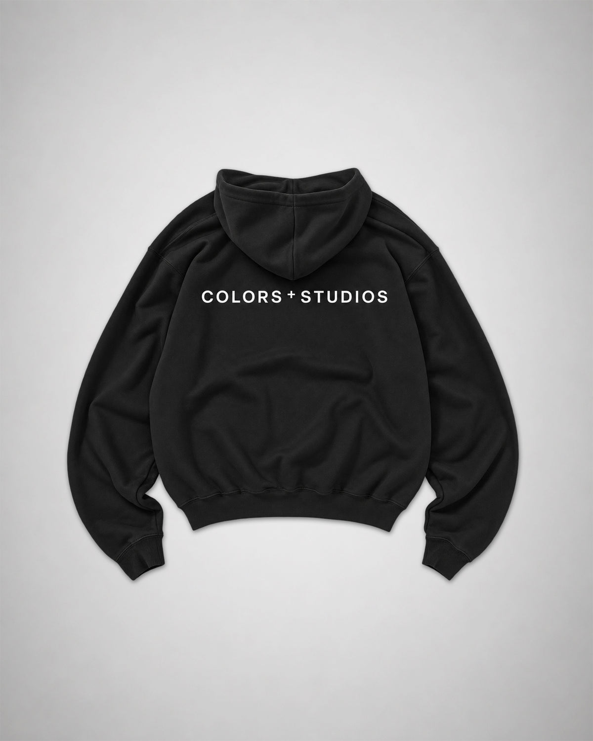 Back view of black COLORS+STUDIOS hoodie with white logo print across the upper back.