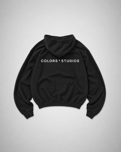 Back view of black COLORS+STUDIOS hoodie with white logo print across the upper back.