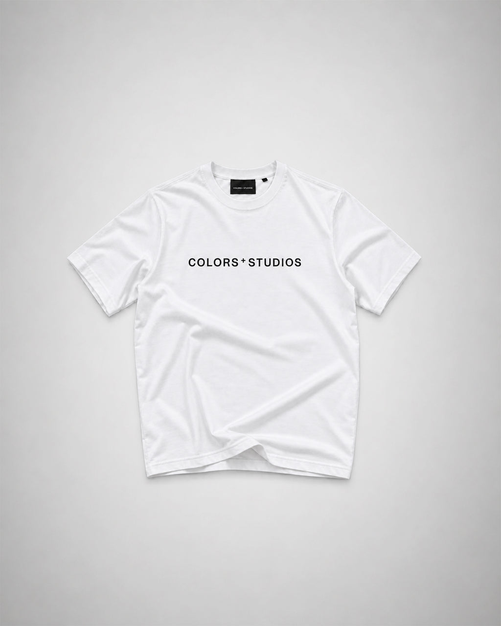 White T-shirt with black COLORS+STUDIOS logo printed across the chest.