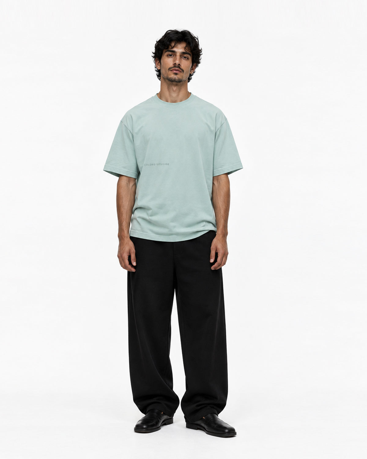 Model in mintgrünem Oversized-T-Shirt mit dezentem Schriftzug auf der Brust, dazu weite schwarze Hose und schwarze Schuhe, Vorderansicht