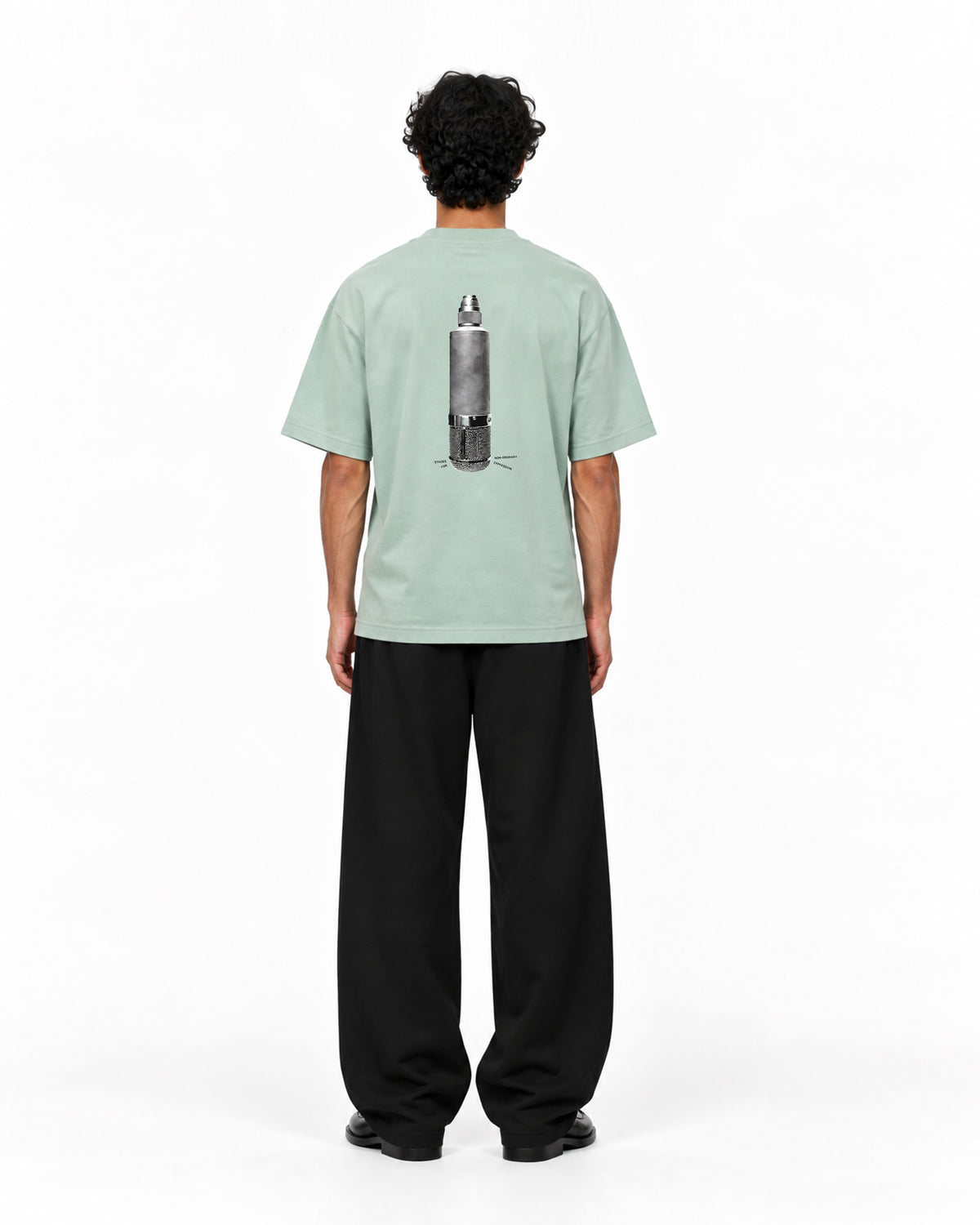 Rückansicht eines Models in mintgrünem Oversized-T-Shirt mit grafischem Schwarz-Weiß-Print eines metallischen Objekts auf dem Rücken, dazu weite schwarze Hose