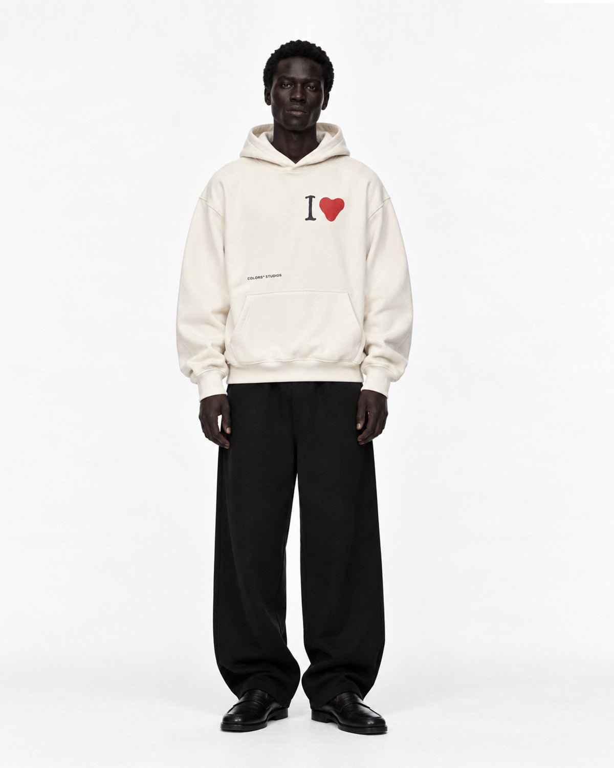 Model in cremeweißem Oversized-Hoodie mit „I ♥“-Print auf der Brust und kleinem Schriftzug, dazu weite schwarze Hose und schwarze Loafer, Vorderansicht