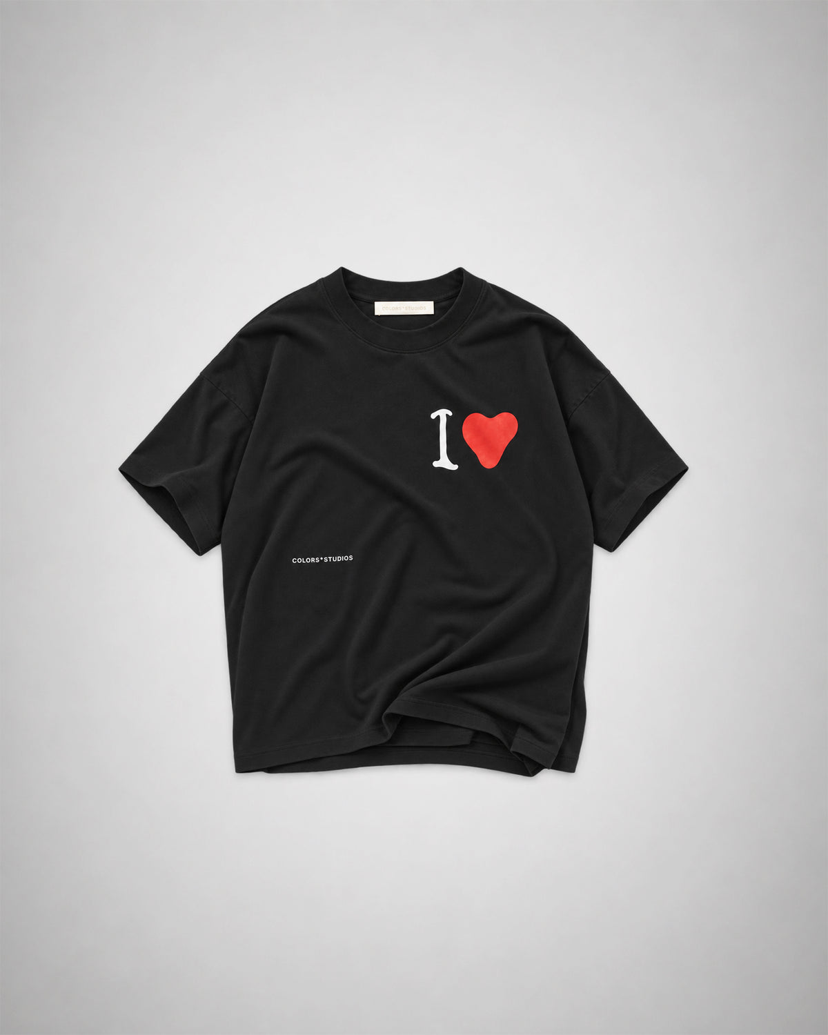 Black oversized T-shirt with white “I” and red heart graphic on the chest and small COLORS*STUDIOS logo.