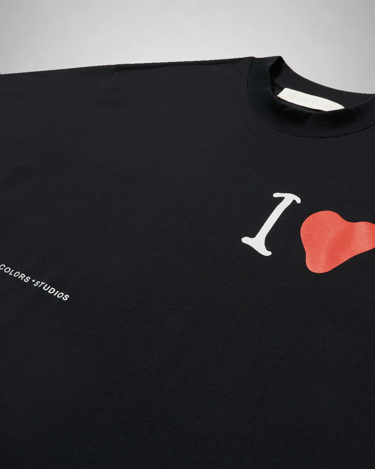 Close-up of the black COLORS t-shirt showing the red heart chest print, the COLORS*STUDIOS wordmark and the woven neck label