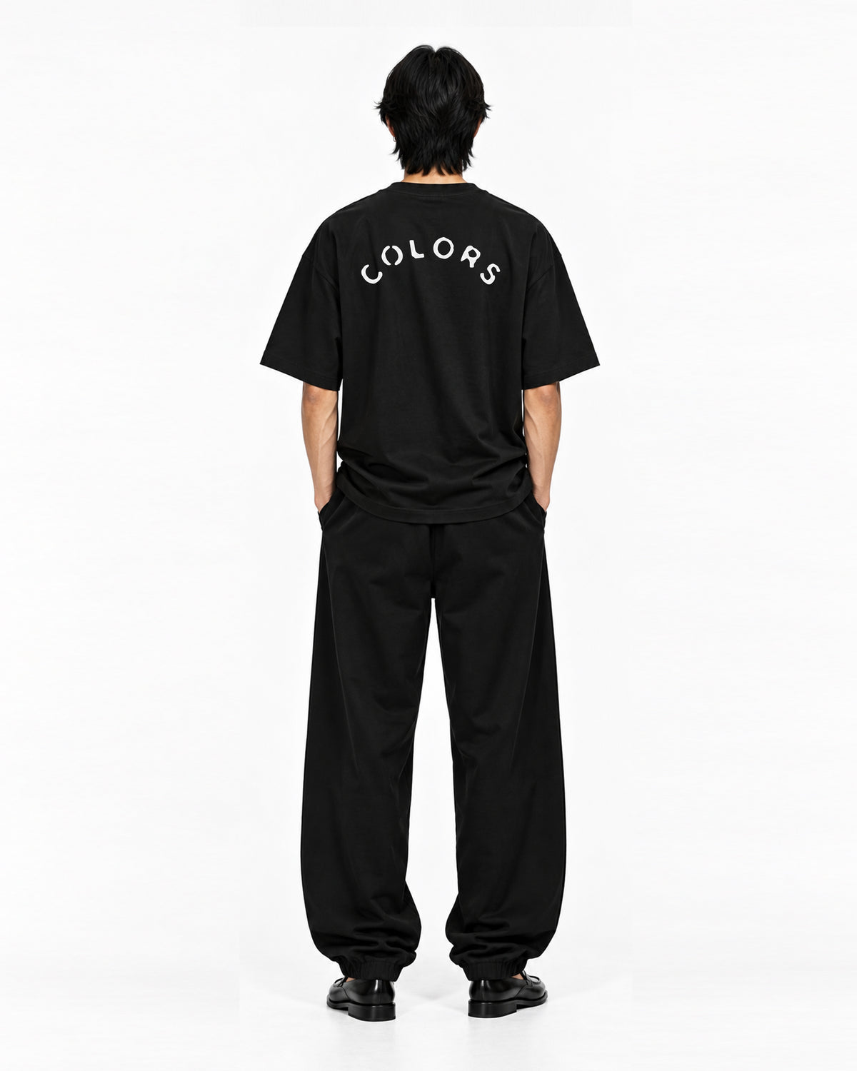 Model seen from behind wearing the black COLORS I Love t-shirt with arched COLORS back print and wide black trousers
